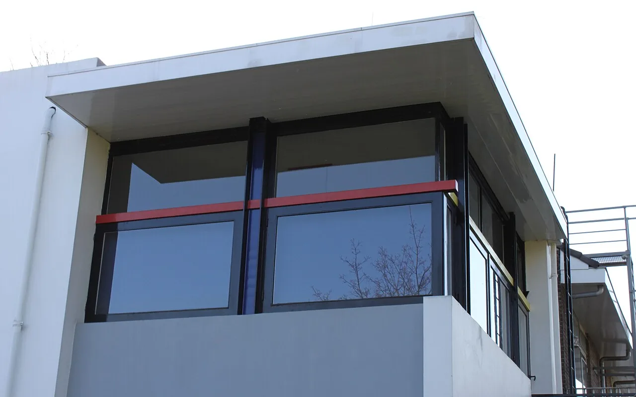 The upper-floor corner window of the Rietveld Schröder House from outside, with red and blue bars across black frames